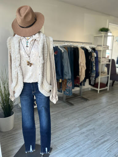 Clothing display at Golden Galleon Boutique - brown Stetson style hat, on white fur coat, with a white shirt, long necklace and blue jeans